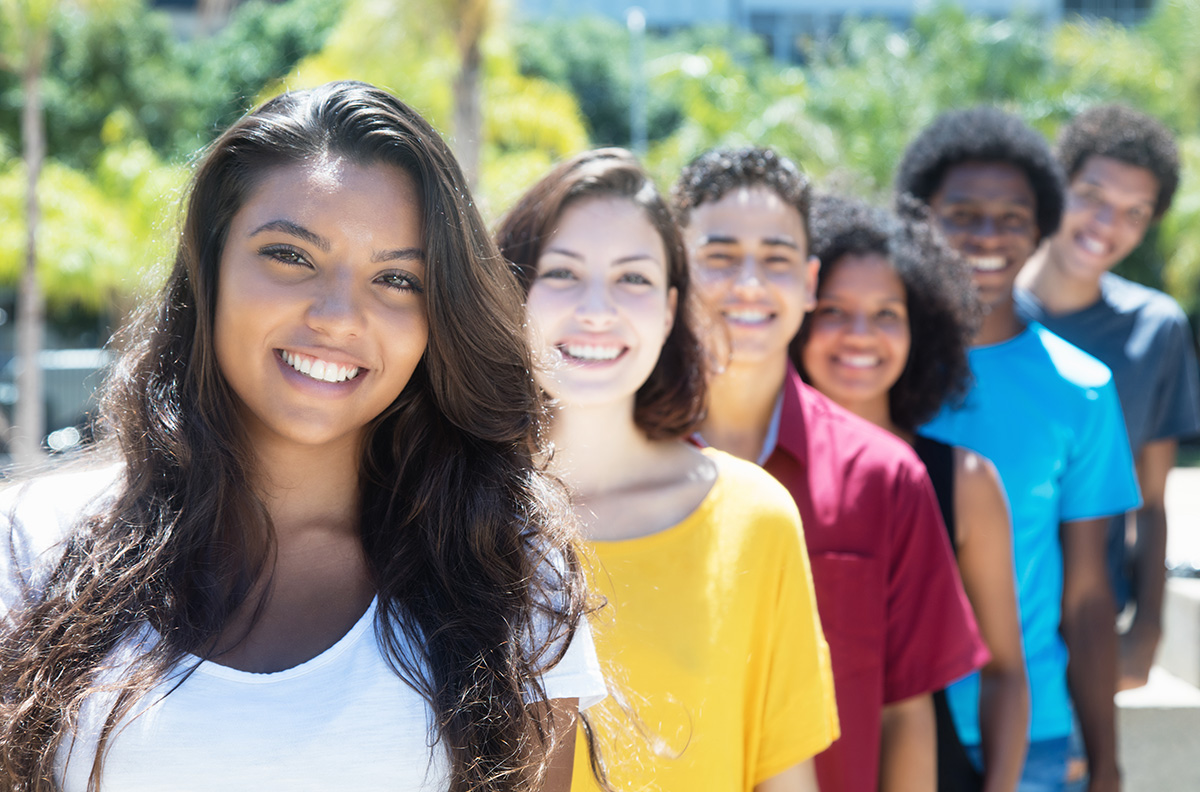 General-Dentistry-Orthodontics-Cooper-Family-Dentistry-Jacksonville, AR-Servicespage-Routine-Dental-Care-Dental-Cleaning Six diverse young people smiling at camera in outdoor setting with green background.