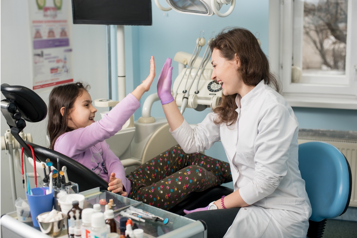 Healthcare provider giving high-five to young patient in medical office during appointment.