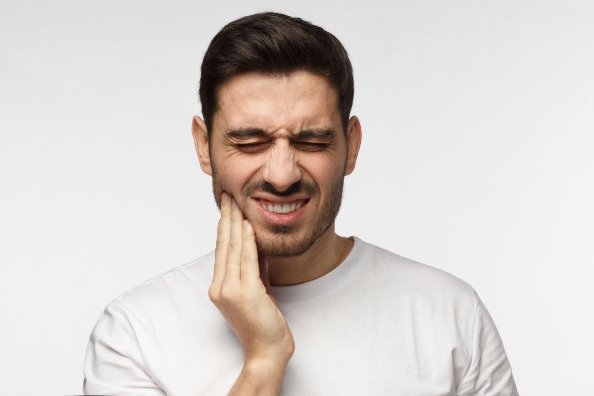 Man in white shirt touching face with hand, smiling against white background
