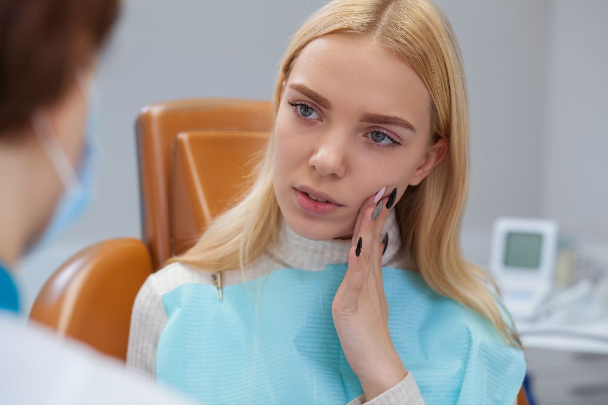 Young woman in blue shirt touching her face during dental consultation with dentist in office.