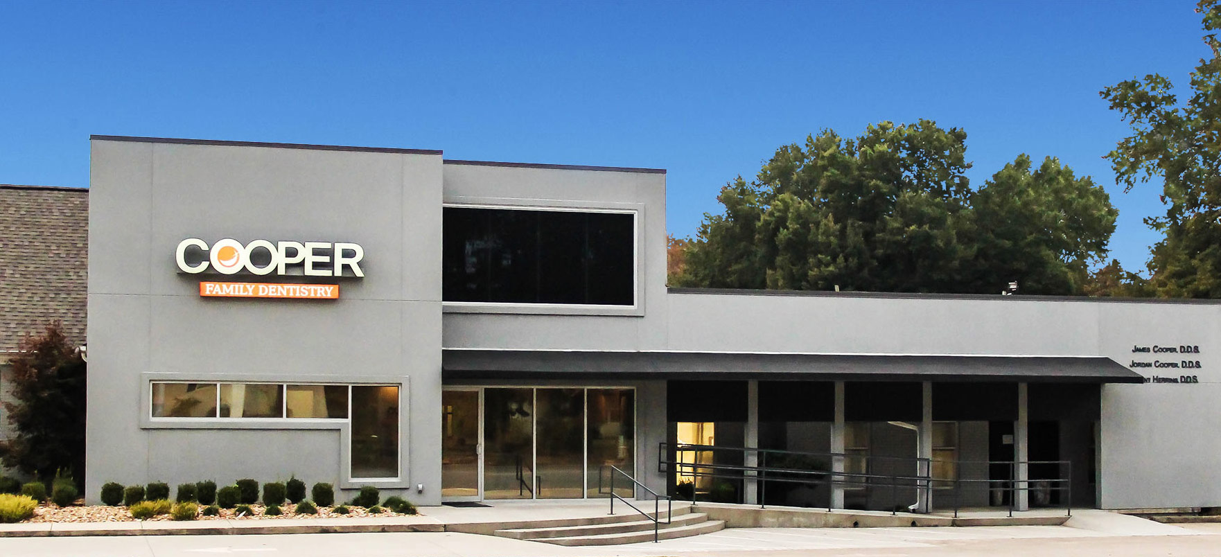 Modern Cooper family storefront building with glass entrance and signage against clear blue sky.