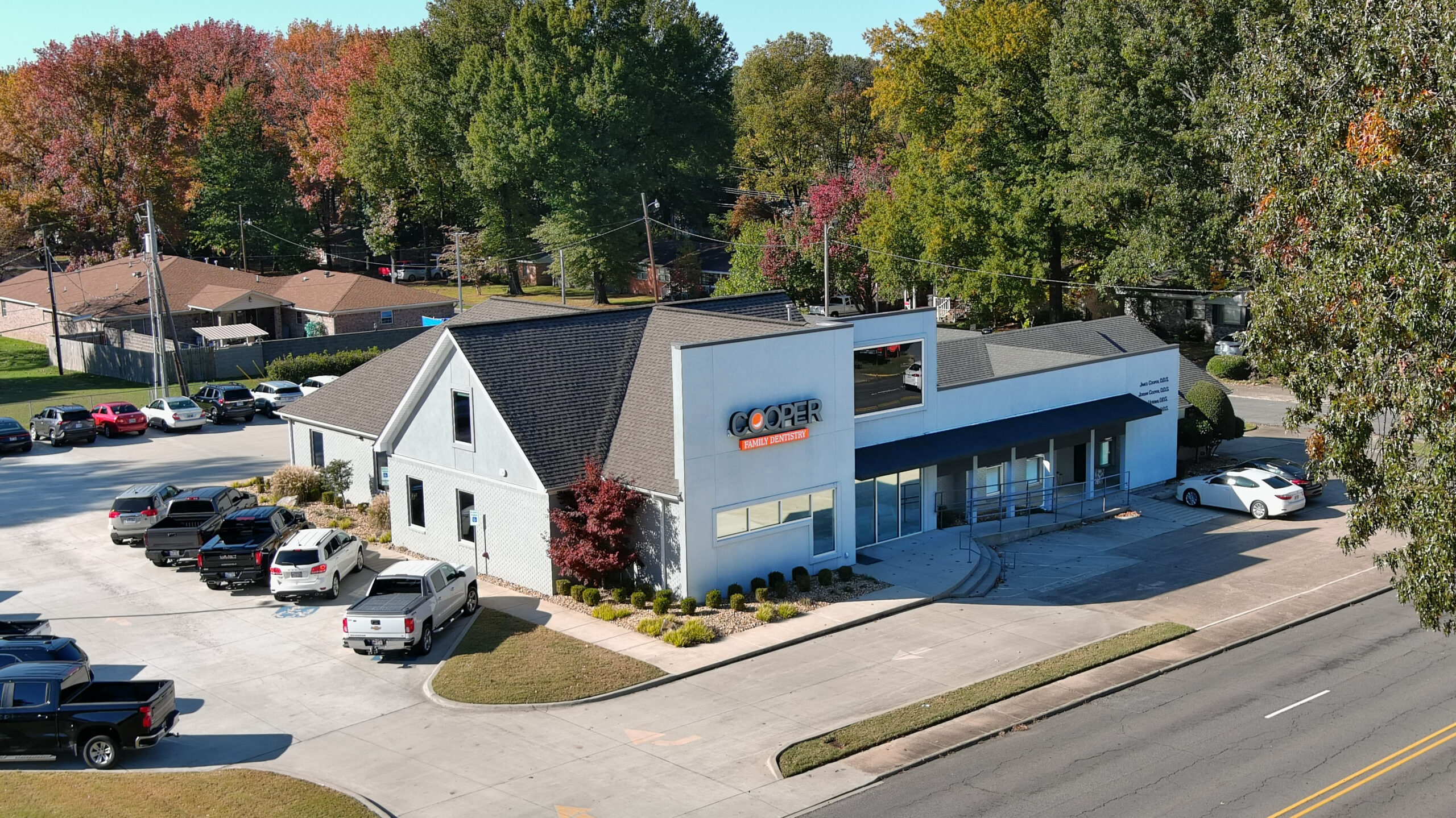 Blue and white commercial building with storefront on corner lot surrounded by parked cars and autumn trees.