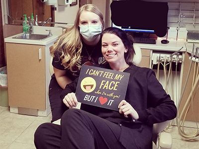 Two women wearing dark clothing pose together in a medical office setting, both smiling at camera.