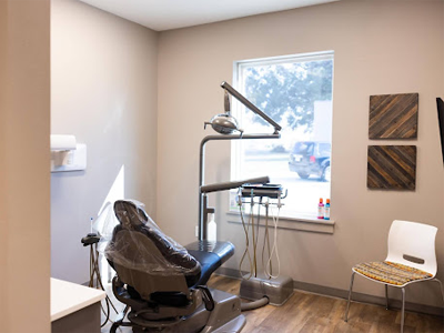 Modern dental operatory with brown chair, overhead light, shelving, and large window in contemporary office.