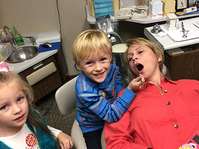 Three young children smiling at camera in home kitchen setting.