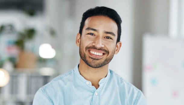 Smiling man in light blue shirt against blurred indoor office background with plants.