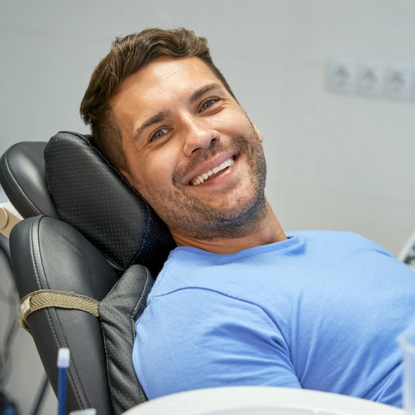 img-IV-sedation-for-deeper-relaxation Man in blue shirt smiling while seated in dental chair at clinic.