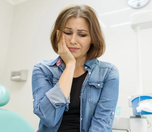 Woman in denim shirt with hand to face, thoughtful expression in bright clinical or medical setting.