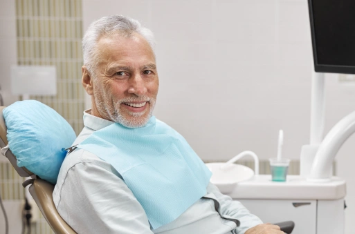 Older man smiling in dental chair wearing bib in modern dental office setting.